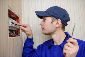 lateral view of a young eletrician in blue overall disassembling a electrical panel with fuses in a house