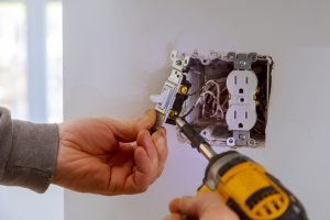 The hands of an electrician installing a power switch to the electrical junction box